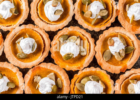 Des plats traditionnels de l'automne. L'Halloween, action de grâce. Ensemble de mini tartelettes à la citrouille épicée en portions individuelles de crème fouettée et de graines de citrouille sur l'onglet de la pierre noire Banque D'Images