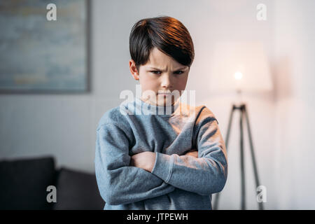 Portrait of boy offensé avec bras croisés looking at camera at home Banque D'Images