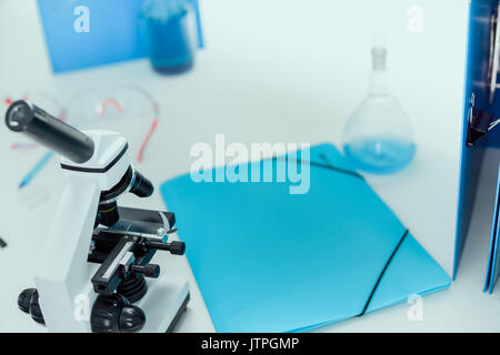 Dossier, tube de réactif bleu et sur la table d'examen au microscope en laboratoire chimique Banque D'Images