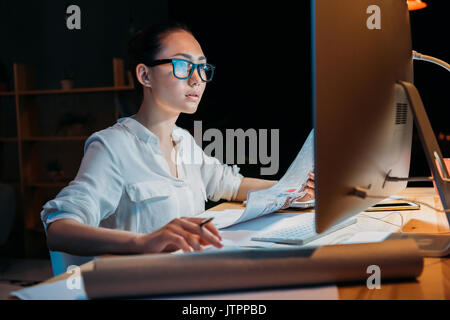 Les jeunes concentrés asian businesswoman in lunettes travailler sur des documents et ordinateur Banque D'Images