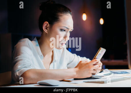 Concentrés asian businesswoman using smartphone, travailler tard au bureau Banque D'Images