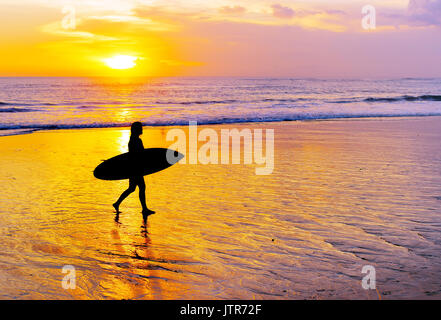 Surfeur femme marchant sur la plage avec une planche de surf au coucher du soleil. L'île de Bali
