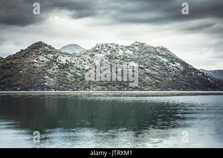 Paysage spectaculaire avec des montagnes à la côte et l'eau tranquille avec réflexion ciel couvert en journée avec ciel dramatique en Europe pays Monténégro Banque D'Images