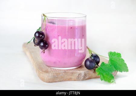 Cocktail de yaourt avec des baies de cassis dans un verre sur une planche de bois. Le bar est décoré avec des bouquets avec des baies de cassis. Side vi Banque D'Images