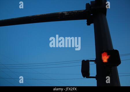 Arrêt lumineux rouge ne marche symbole main sur feu de circulation à l'intersection avec l'après les lignes d'énergie électrique à l'arrière-plan après le crépuscule contre Ciel Bleu clair Banque D'Images