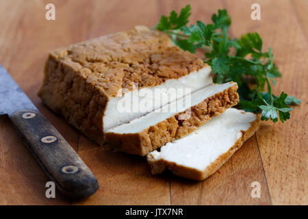 Bloc de tofu fumé, deux tranches de tofu, couteau rustique et persil frais sur planche en bois. Banque D'Images