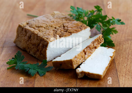 Bloc de tofu fumé, deux tranches de tofu et de persil sur planche en bois. Banque D'Images
