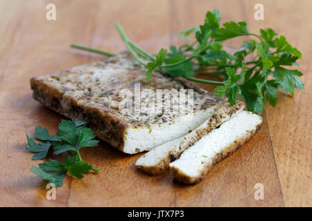 Bloc de tofu mariné aux herbes, deux tranches de tofu et de persil sur planche en bois. Banque D'Images