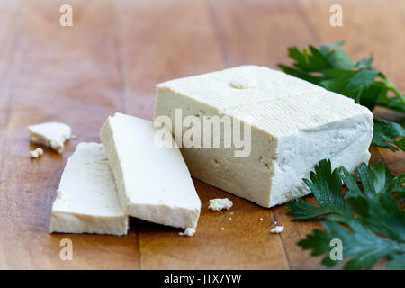 Un bloc de tofu blanc avec deux tranches de tofu, miettes et persil frais sur planche en bois. Banque D'Images