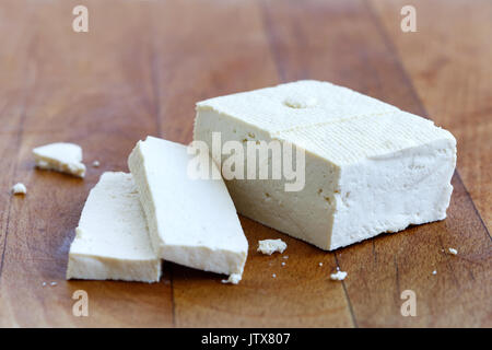 Un bloc de tofu blanc et deux tranches de tofu avec des miettes sur planche en bois. Banque D'Images