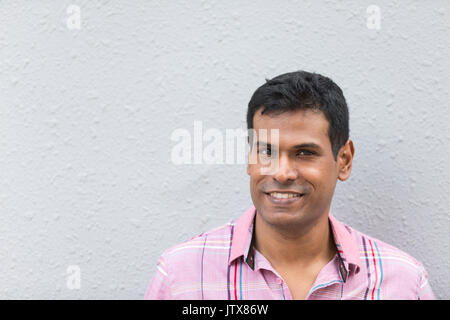 L'homme indien s'appuyant sur un mur gris. Beau jeune homme asiatique appuyé contre un mur gris et regardant la caméra Banque D'Images