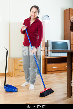 Mature femme au foyer avec pelle et brosse de nettoyage dans la salle de séjour à la maison Banque D'Images