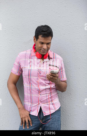 L'homme indien avec un téléphone intelligent. Asian man using Smart Phone, appuyé contre un mur gris. Banque D'Images
