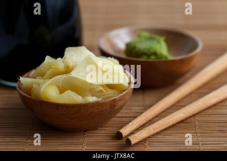 Tranches de gingembre mariné dans bol en bois de bambou à côté de baguettes, la pâte de wasabi et bouteille de sauce soya. Banque D'Images