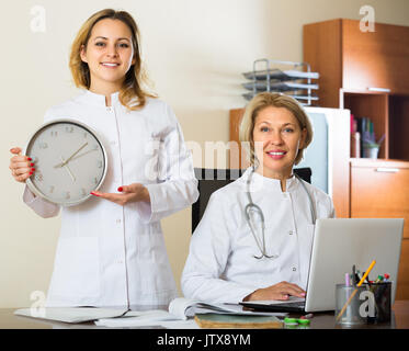 Deux femmes médecins holding clock and smiling in clinique moderne Banque D'Images