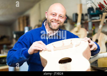 Fabricant de guitares avec succès dans une procédure d'une guitare acoustique dans un atelier. Il est à la recherche de l'appareil photo et le cas de guitare cheking Banque D'Images