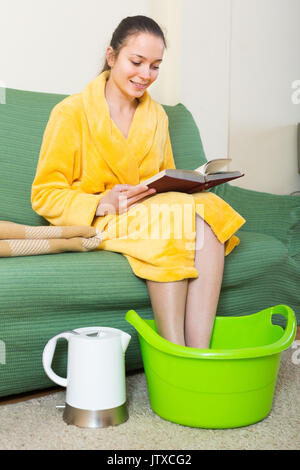 Jeune femme positive en peignoir assis avec pieds en basin Banque D'Images