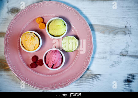 Sélection de saveurs gastronomiques de glaces italiennes dans des couleurs vibrantes servi dans des tasses en porcelaine sur une vieille table en bois rustique dans un glacier, angle view jpg Banque D'Images