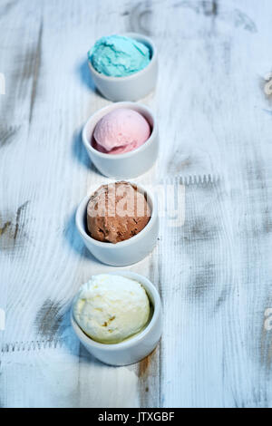 Sélection de saveurs gastronomiques de glaces italiennes dans des couleurs vibrantes servi dans des tasses en porcelaine sur une vieille table en bois rustique dans un glacier, angle view jpg Banque D'Images