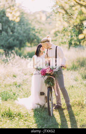 La photo de la couple transportant la location avec les fleurs roses et les baisers dans le domaine en vert. Banque D'Images