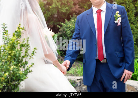 Jeunes mariés le jour de leur mariage. Close-up of groom's hand holding bride's wirst tendres. Wedding couple appréciant les moments romantiques dans le jardin. Banque D'Images