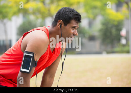 Portrait de l'homme Indien athlétique se reposant après ruissellement urbain à travers les rues de la ville. Asian male runner en tenant debout pause détente. Banque D'Images