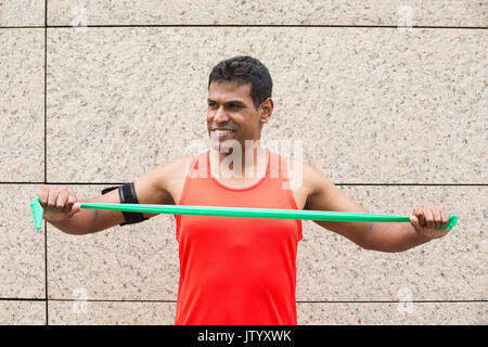 Portrait d'un homme Indien athlétiques à l'aide de bandes stretch à l'extérieur en milieu urbain. Banque D'Images