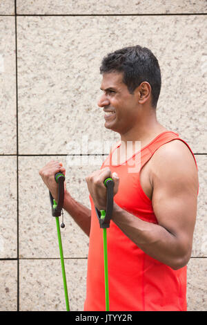 Portrait d'un homme Indien athlétiques à l'aide de bandes stretch à l'extérieur en milieu urbain. Banque D'Images