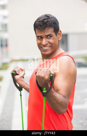 Portrait d'un homme Indien athlétiques à l'aide de bandes stretch à l'extérieur en milieu urbain. Banque D'Images