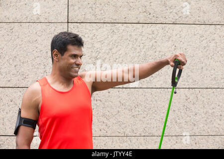 Portrait d'un homme Indien athlétiques à l'aide de bandes stretch à l'extérieur en milieu urbain. Banque D'Images