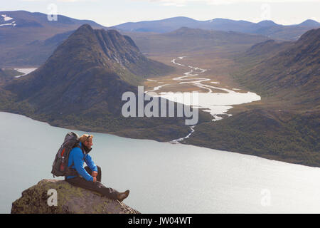 Un randonneur jouit de la vue sur les fjords et les montagnes tout en étant assis sur un rocher de la fameuse crête de Besseggen en Norvège. Cette traverse un jour dans le parc national de Jotunheimen est le sentier de randonnée le plus populaire en Norvège. Banque D'Images