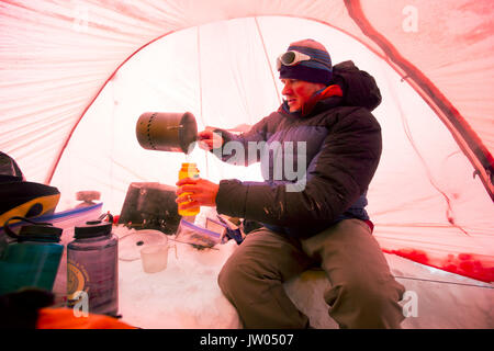 Un des alpinistes est la fonte de la neige pour obtenir de l'eau potable, à l'intérieur d'une tente au camp de Denali en Alaska. Tôt le matin, ils vont d'un sommet à pousser la plus haute montagne d'Amérique du Nord. Banque D'Images