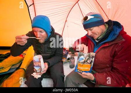 Deux alpinistes mangent des aliments déshydratés à l'intérieur d'une tente au camp de Denali en Alaska. Tôt le matin, ils vont d'un sommet à pousser la plus haute montagne d'Amérique du Nord. Banque D'Images