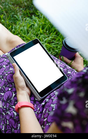 Femme anonyme dans white hat et robe de détente sur l'herbe verte avec tablette. Vue arrière. Petit coup à orientation verticale modèle de vue. Banque D'Images