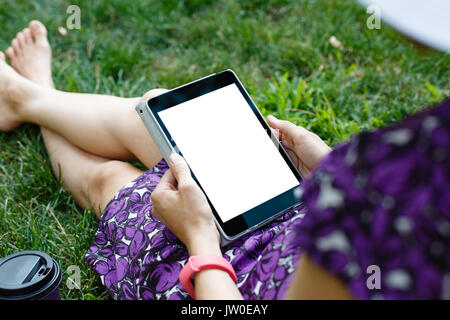 Femme anonyme dans white hat et robe de détente sur l'herbe verte avec tablette. Vue arrière. Petit coup à orientation verticale modèle de vue. Banque D'Images