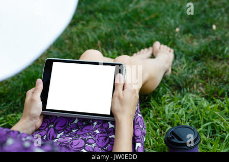 Femme anonyme dans white hat et robe de détente sur l'herbe verte avec tablette. Vue arrière. Petit coup à orientation verticale modèle de vue. Banque D'Images