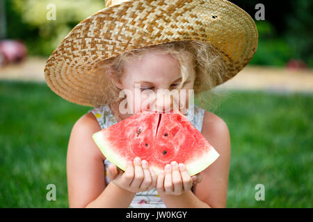 Petite fille au chapeau de paille avec de grandes tranche de pastèque assis sur l'herbe verte en été park Banque D'Images