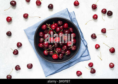 Cerise sucrée fraîche dans un bol noir sur fond de béton gris. Vue de dessus de table Banque D'Images