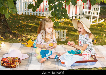 Deux petites filles assis sur l'herbe verte et manger ensemble contre green lawn Banque D'Images