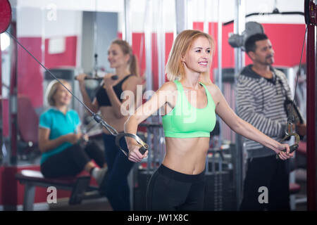 Groupe de femmes et d'homme ayant un entraînement intensif sur des machines de sport club Banque D'Images