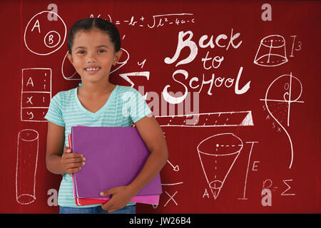 Portrait of smiling girl holding files contre blackboard with copy space sur planche de bois Banque D'Images
