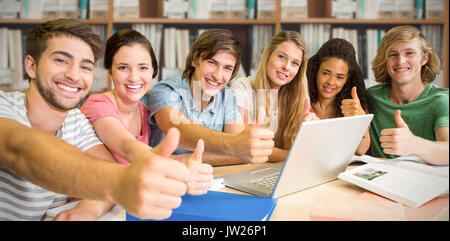 Les étudiants du collège gesturing Thumbs up in library contre divers multi colored books on shelf Banque D'Images