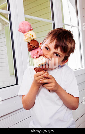 Photo d'un enfant de 6 ans mange d'un grand cornet de crème glacée avec six boules de chocolat, vanille et fraise. Banque D'Images