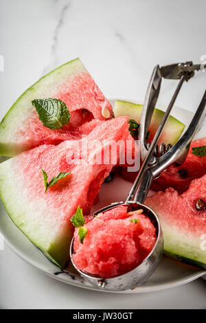 Desserts de fruits d'été, les cocktails. La crème glacée en granit de pastèque à la menthe, un scoop en cuillère pour la crème glacée, sur la plaque avec des tranches de waterm Banque D'Images