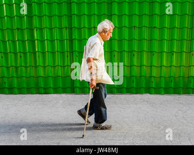 Un mâle Hispanic Senior citizen marche avec une canne à côté d'un mur fait de vert vif de tuiles produisant une répétition de la forme dans la Havane, Cuba. Banque D'Images