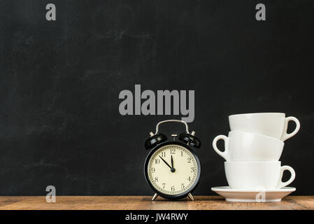 Tasses à café blanches empilées avec réveil rétro sur tableau noir wall background montrant style design sur table en bois sol avec copyspace publicité. Banque D'Images