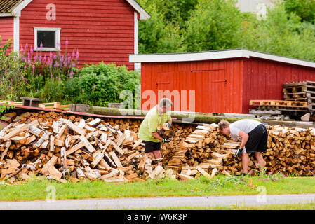 Lindesnes, Norvège - 1 août 2017 : Voyage de deux hommes documentaire bois empilage en dehors de leur maison. Les énergies renouvelables produites localement biocarburant solide est ofte Banque D'Images