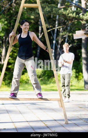 Toute la longueur de mature woman smiling sur structure en bois alors que ami tirant des cordes attachées sur patio Banque D'Images