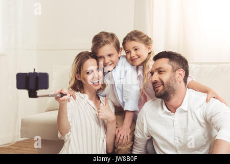Famille heureuse en tenant sur smartphone selfies avec monopode à la maison Banque D'Images