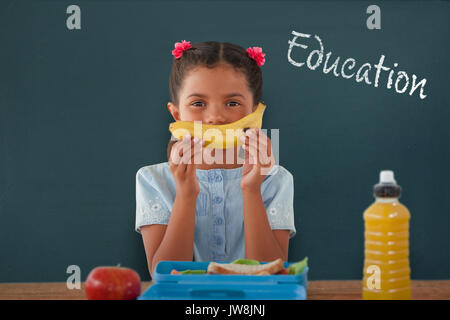 Girl holding banana à table contre l'éducation texte contre fond blanc Banque D'Images